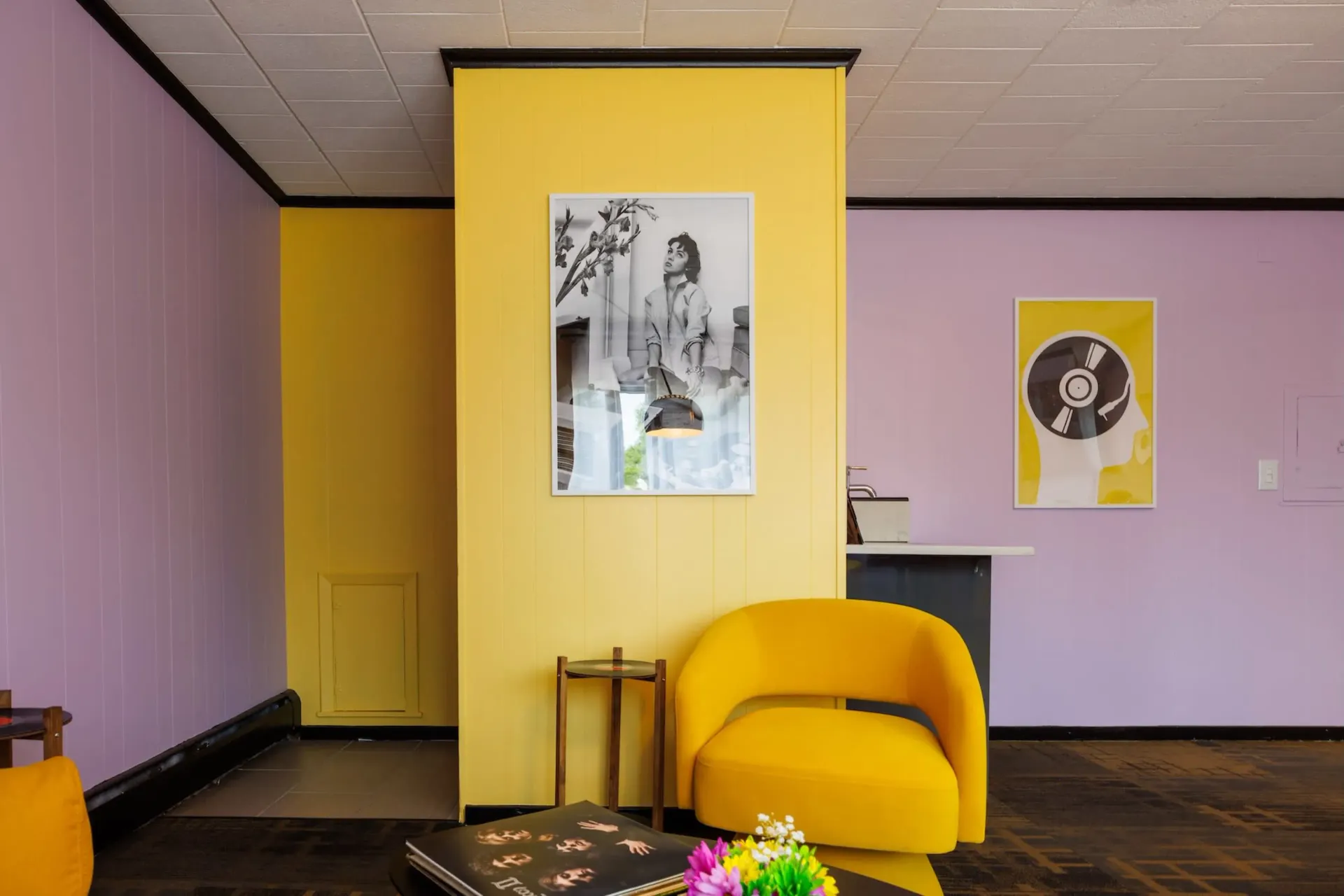 Colorful modern room with yellow chair, lavender walls, yellow partition, and framed black-and-white art.