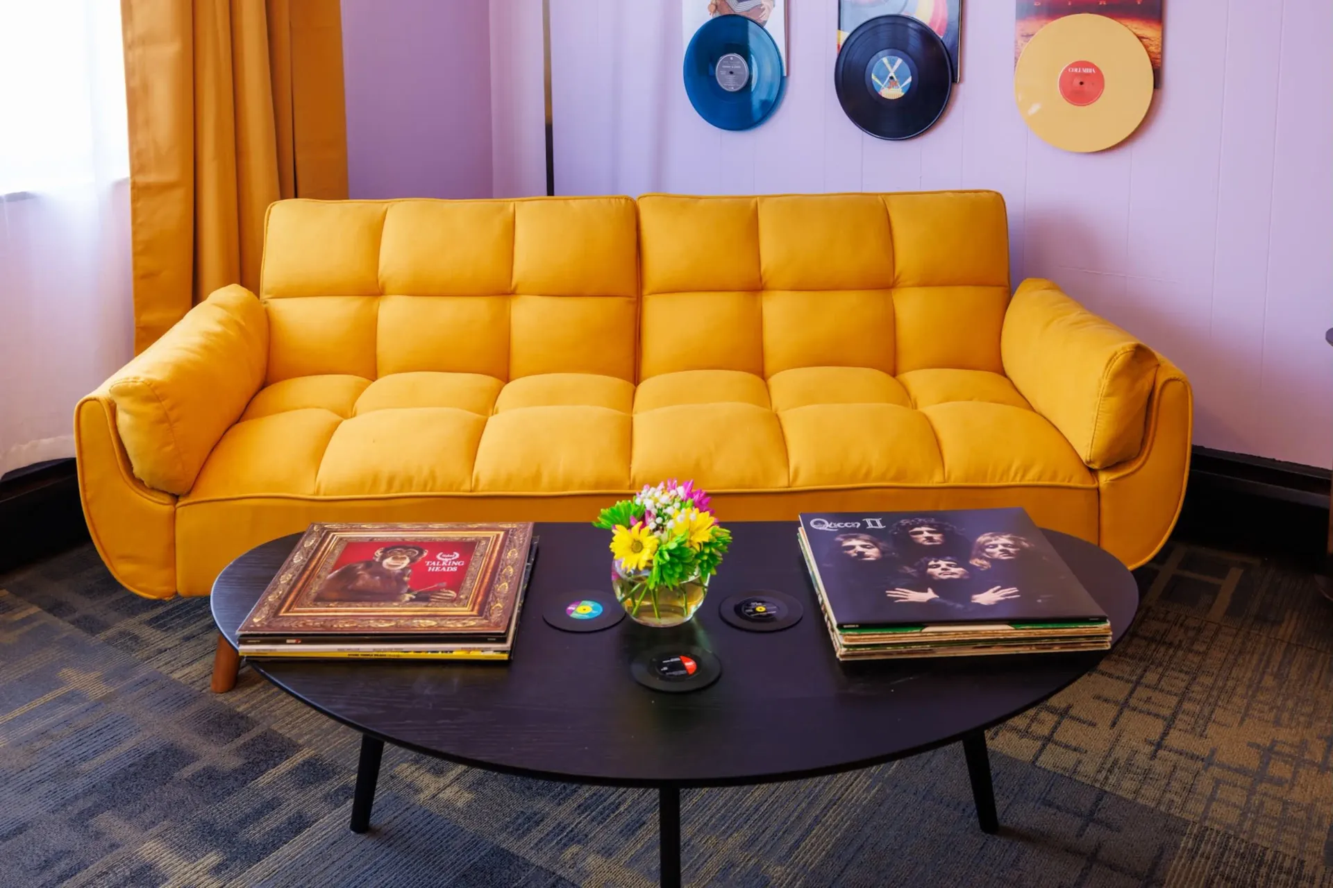 Yellow sofa in a cozy living room with vinyl wall art and a black coffee table with books and flowers