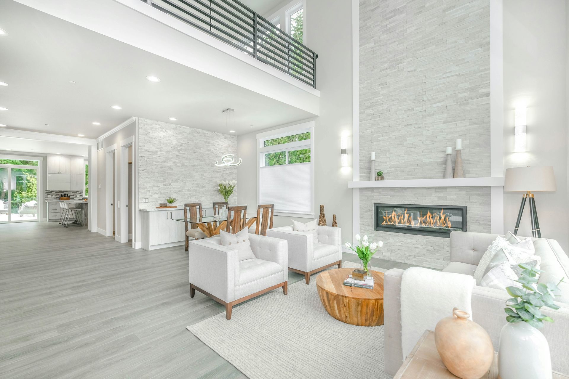 Bright modern living room with white furniture, high ceiling, fireplace, and balcony railing