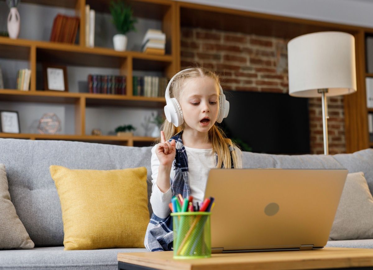 Child wearing headphones studies at a laptop on a couch in a cozy living room.
