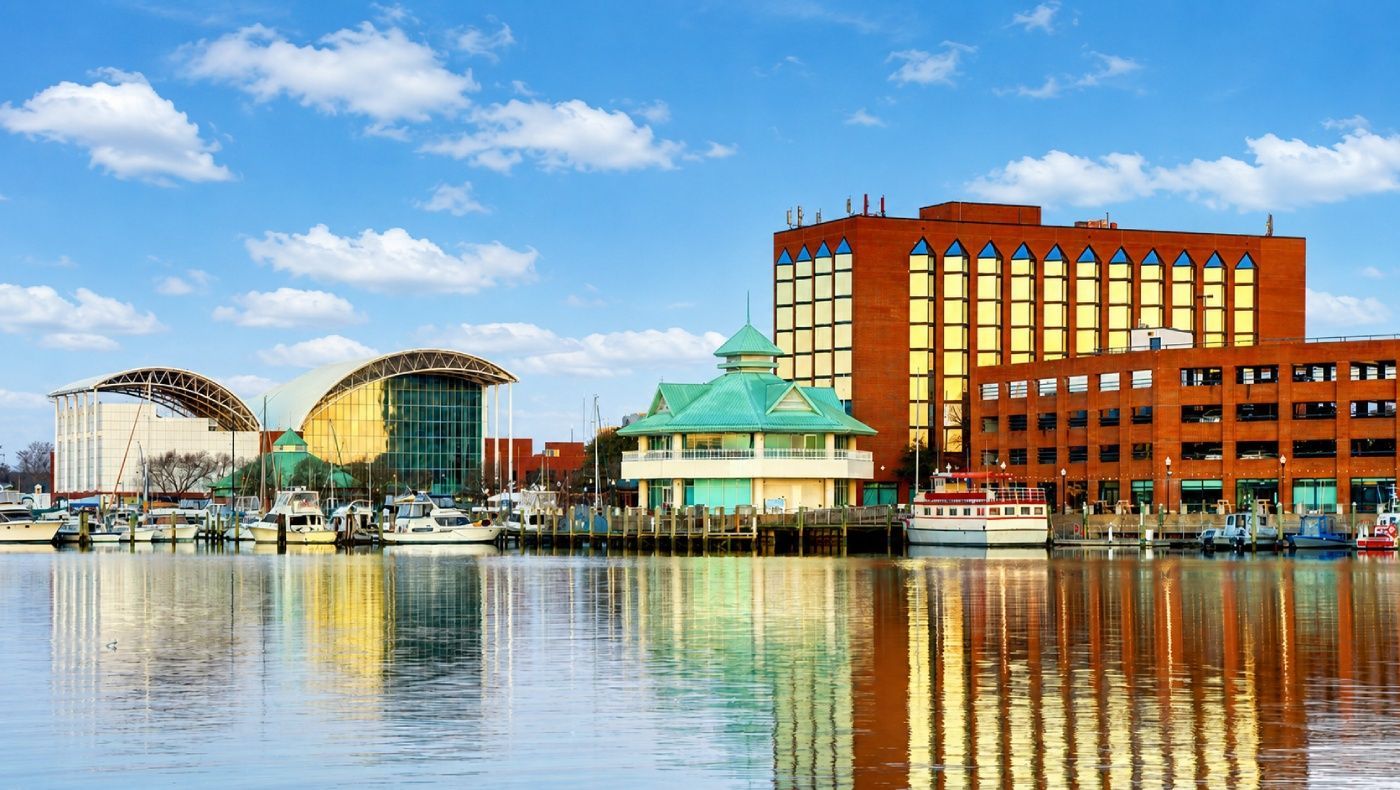 Waterfront marina with colorful buildings and their reflections in calm water.
