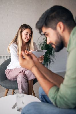 Woman smiling at a tablet while a man in the foreground looks at a phone in a bright living room