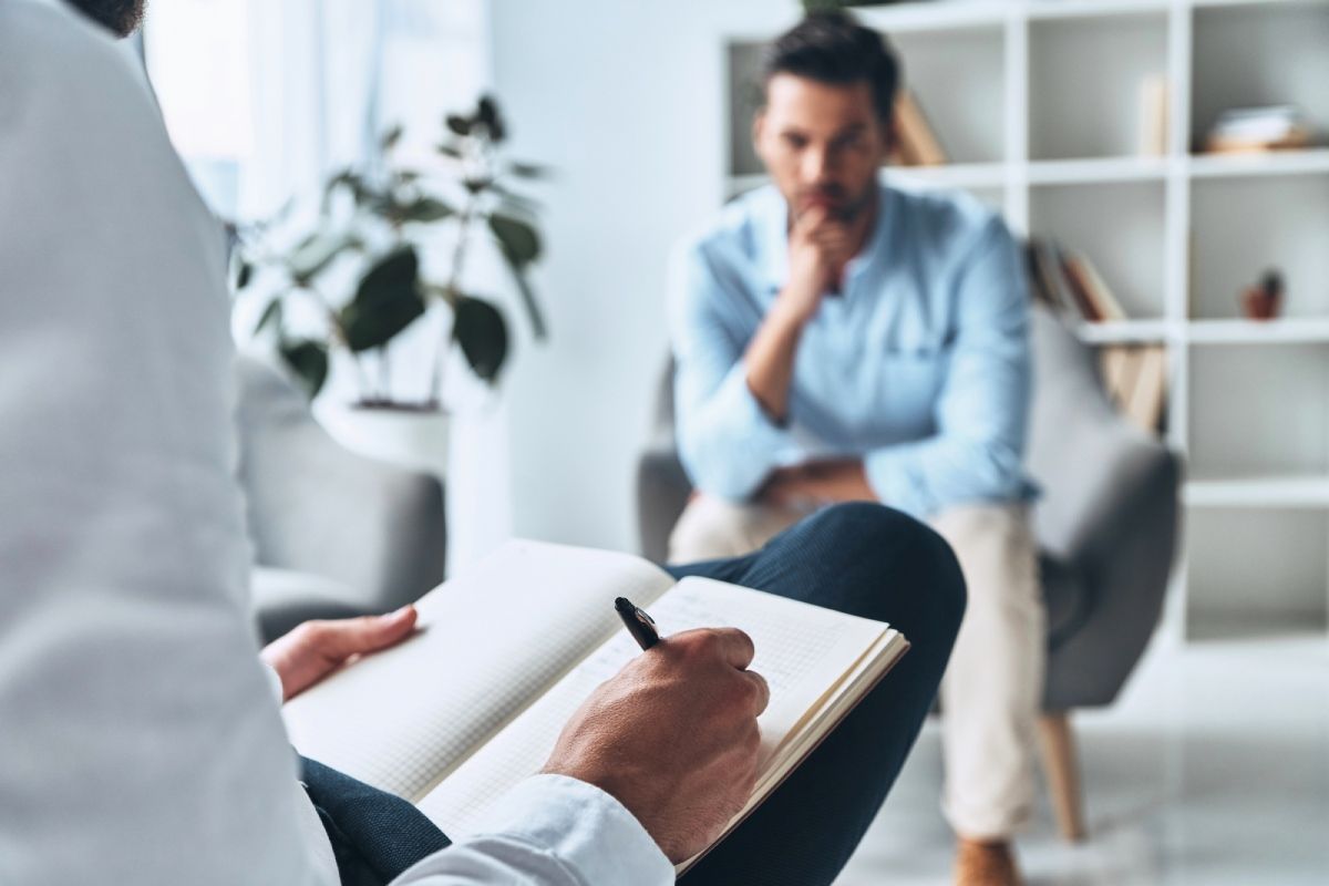 Therapist taking notes while speaking with a seated client in a bright office