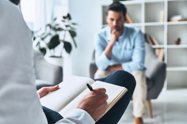 Therapist taking notes while speaking with a seated client in a bright office