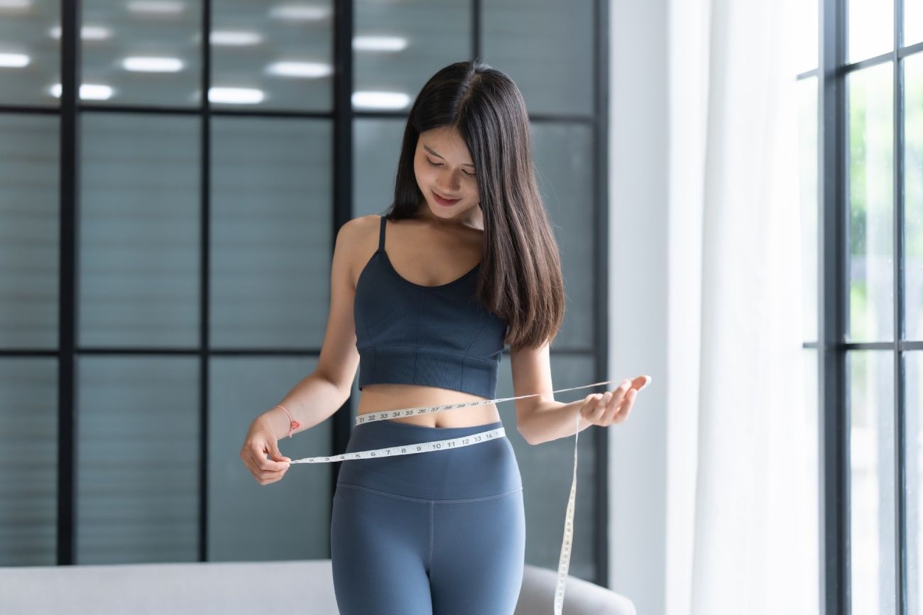 Woman in black athletic wear standing indoors, smiling in a bright modern room