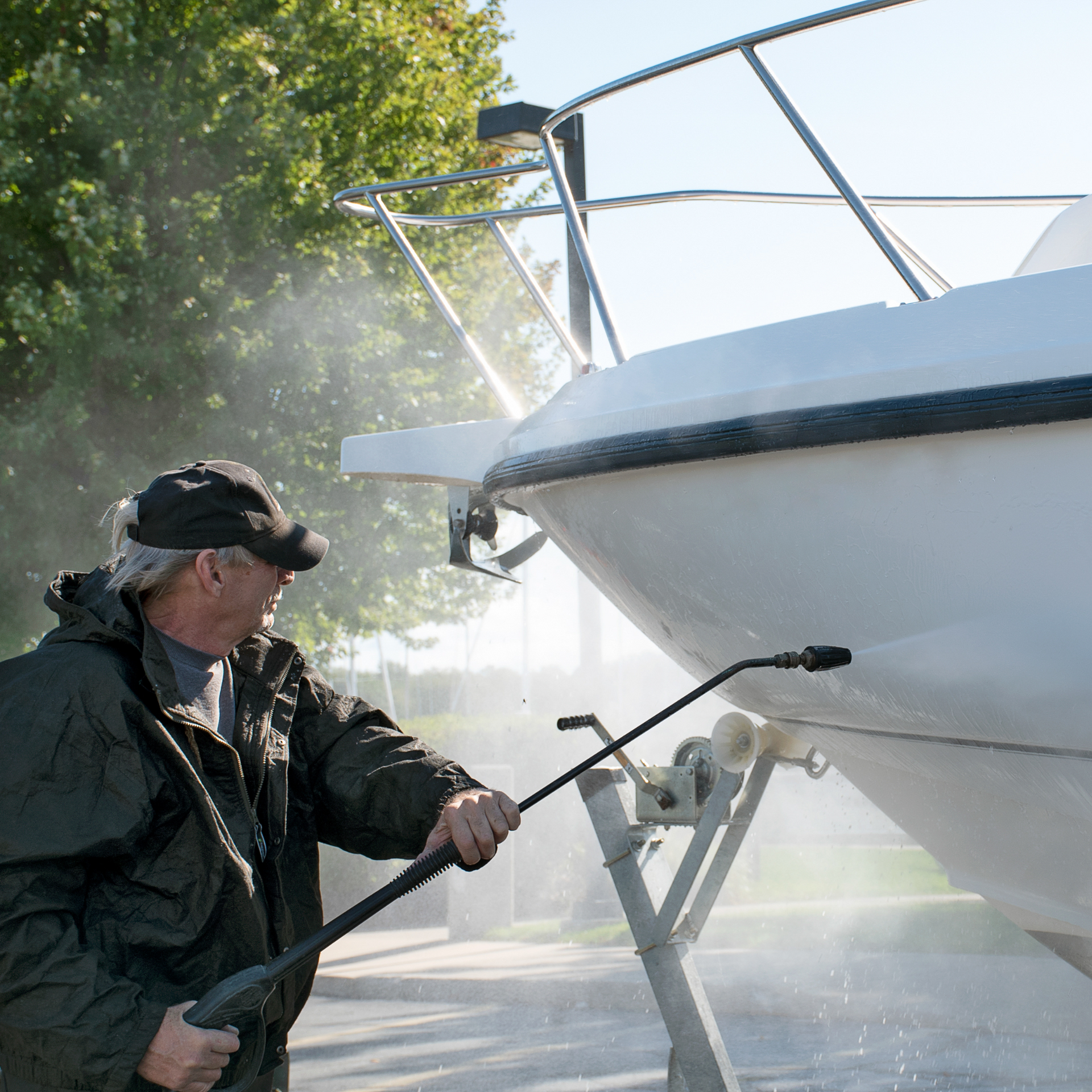 Man power washing a white boat, spraying water.