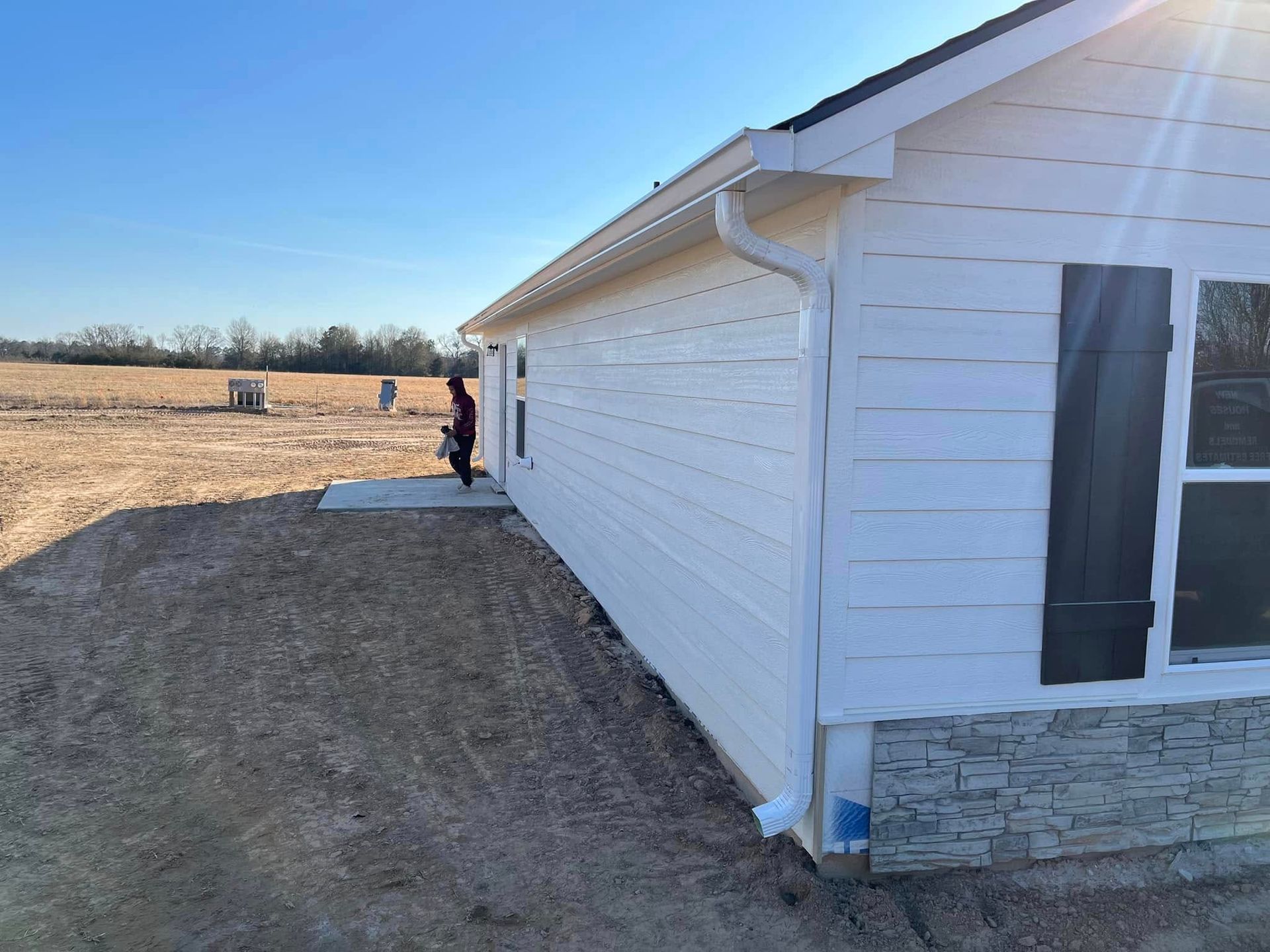 White house exterior with a person standing by the side wall in a rural field