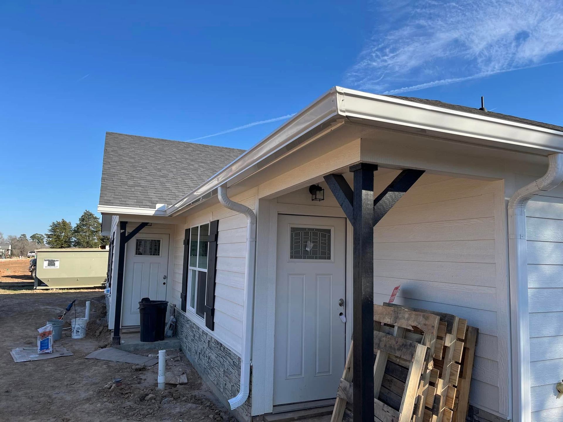 House exterior with white siding, gray roof, and front porch under construction on a clear day