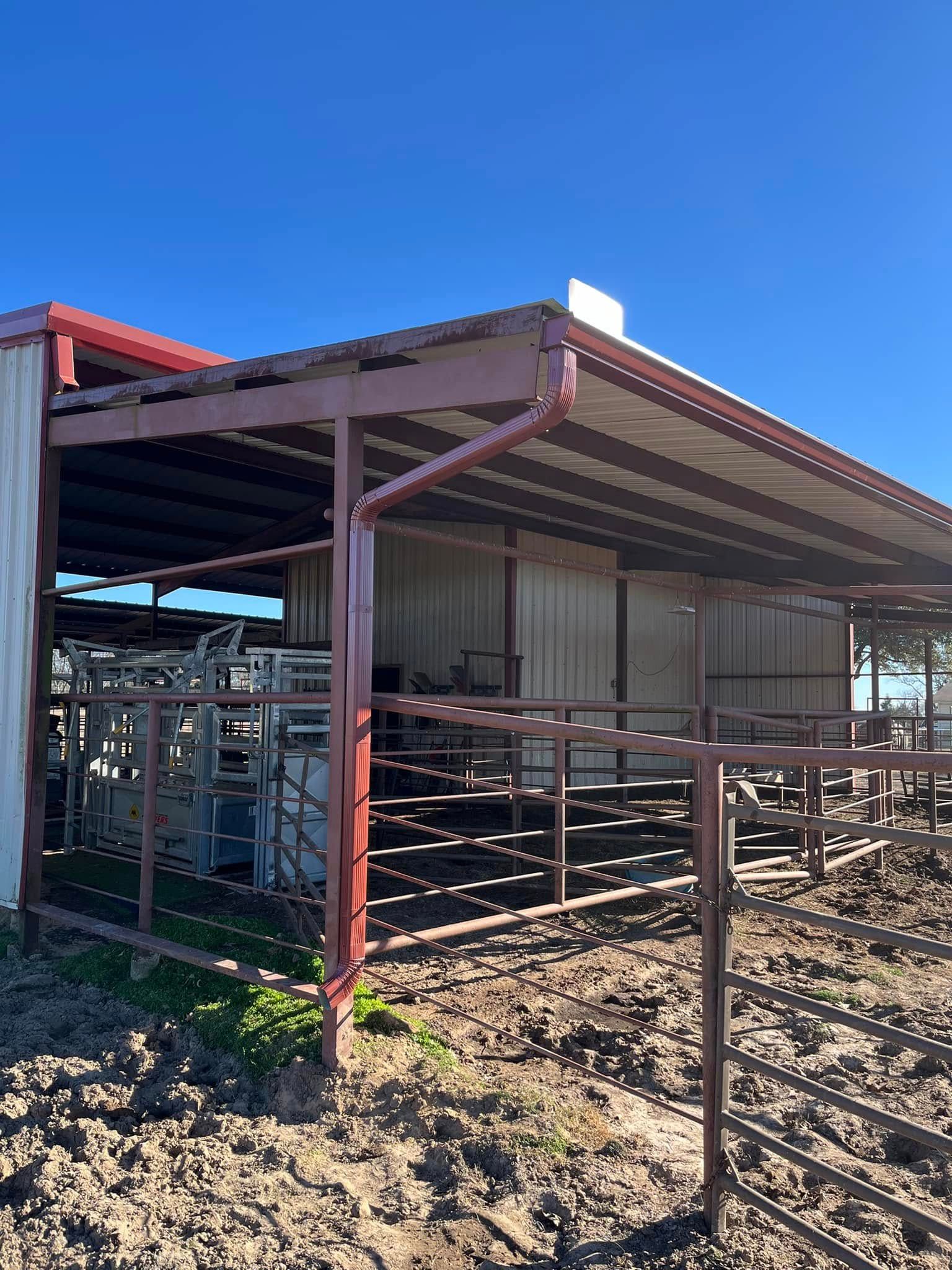 Rusty steel livestock pen and shed under construction on muddy ground beneath a clear blue sky