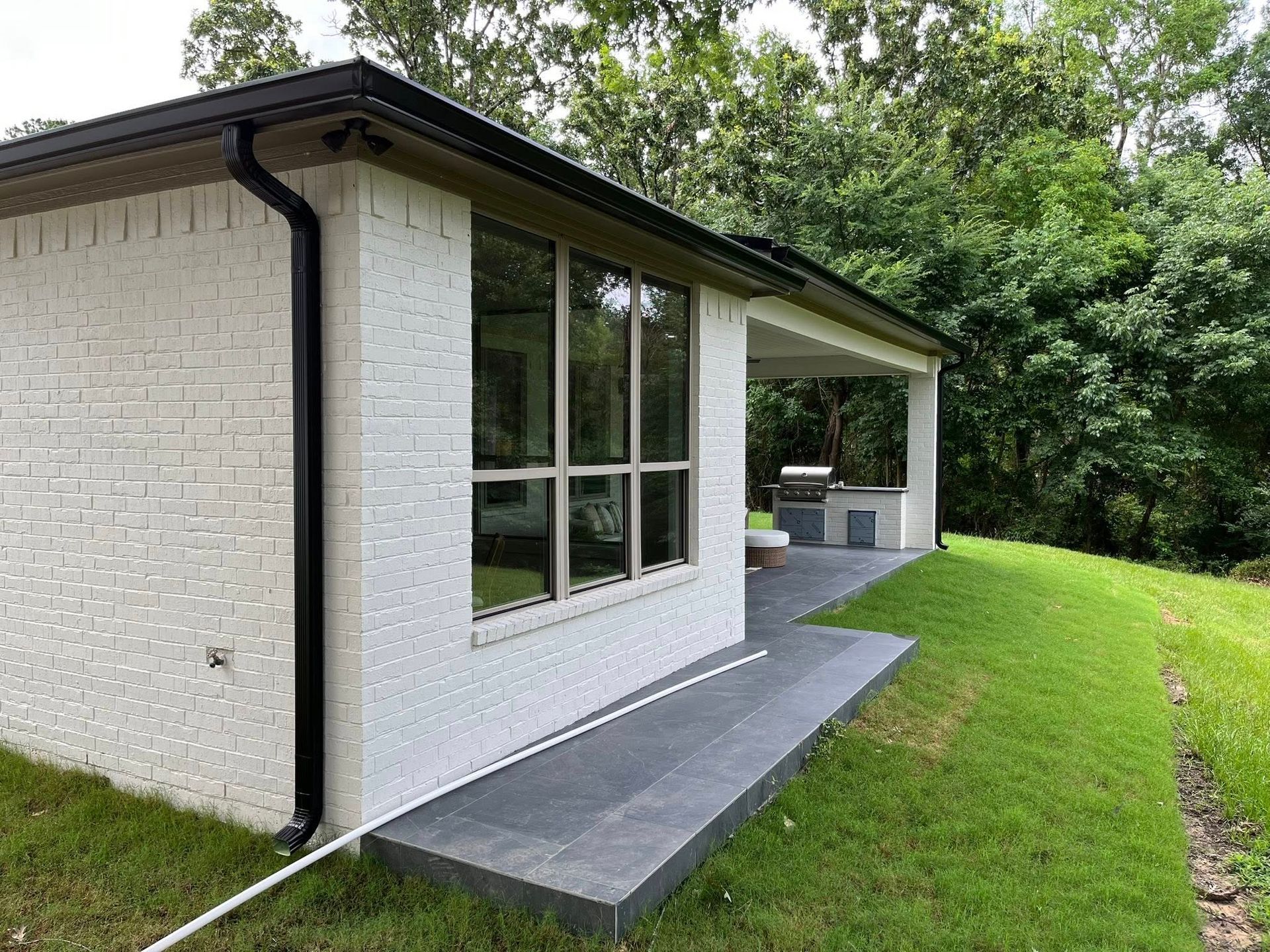Side view of a white house with a gray accessible ramp leading to a covered patio and green lawn.
