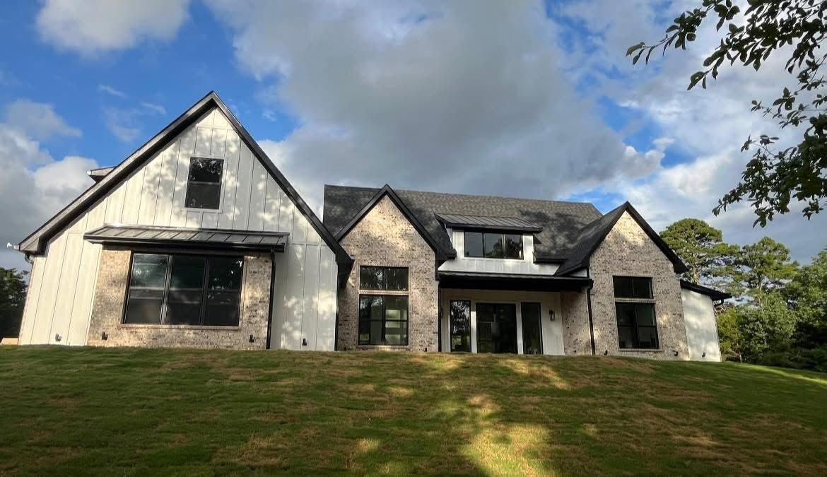 Large white house with dark roof, front porch, and grassy lawn under a partly cloudy sky