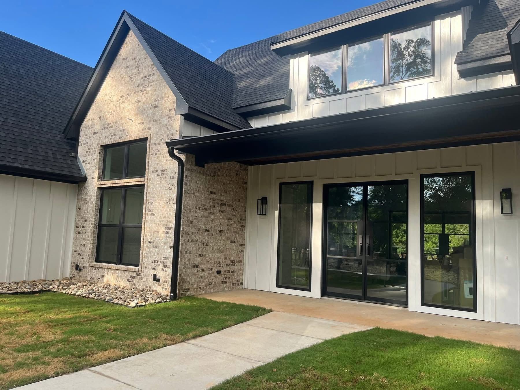 Modern two-story house exterior with stone and white siding, black-framed windows, and a covered patio