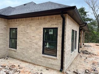 Brick house exterior under construction with black roof, windows, and unfinished dirt surrounding it