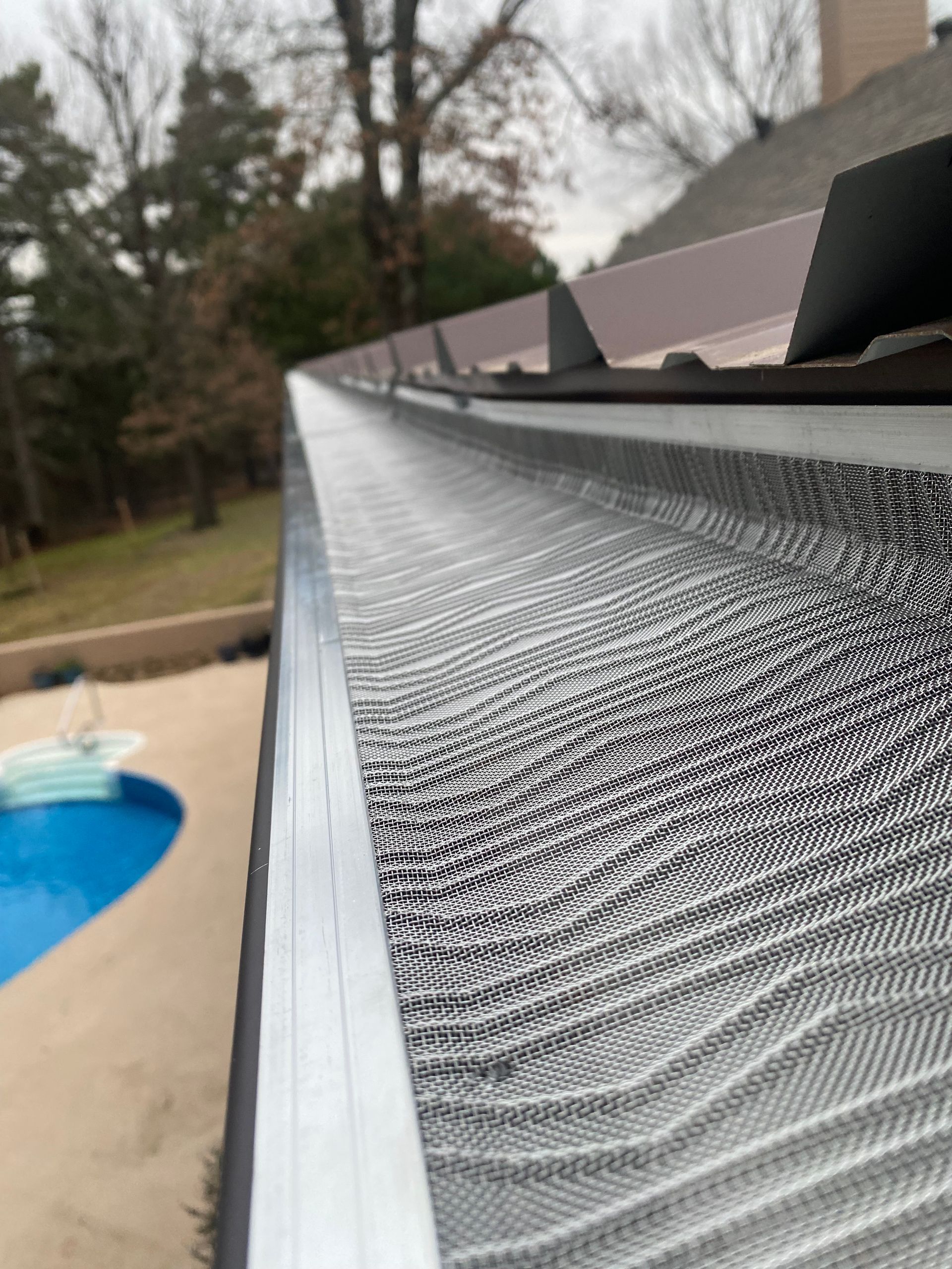 Roof eave with aluminum gutter guard, viewed along the edge beside a backyard pool