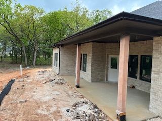 Partially built house with a covered porch and brick columns beside a wooded lot
