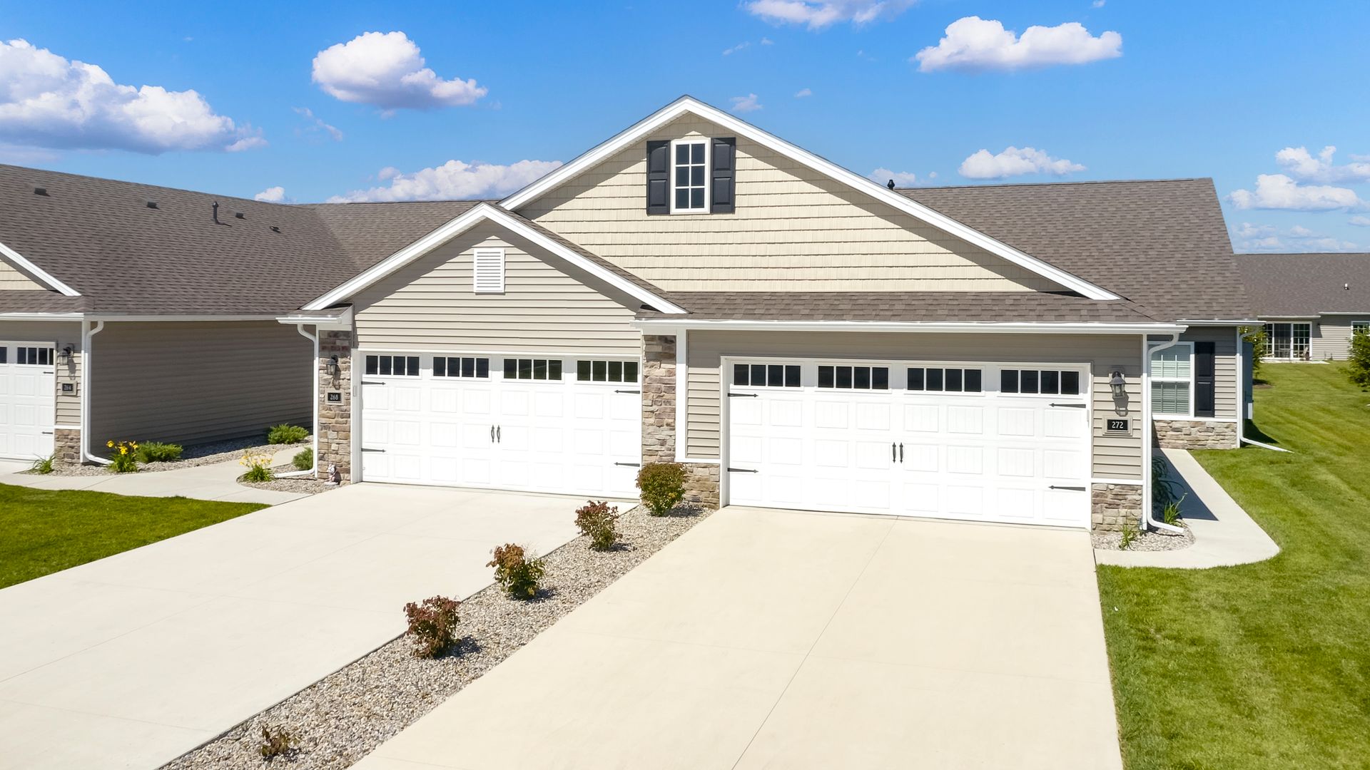Townhomes with white garage doors, stone accents, and brown roofs, under a blue sky.