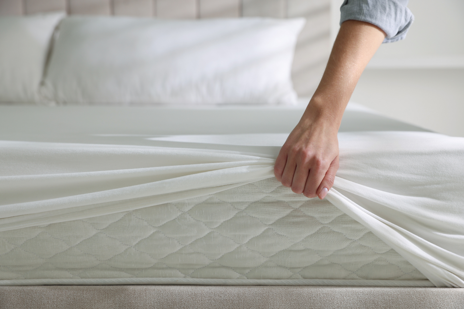 Hand lifting a white sheet to reveal a mattress topper on a bed
