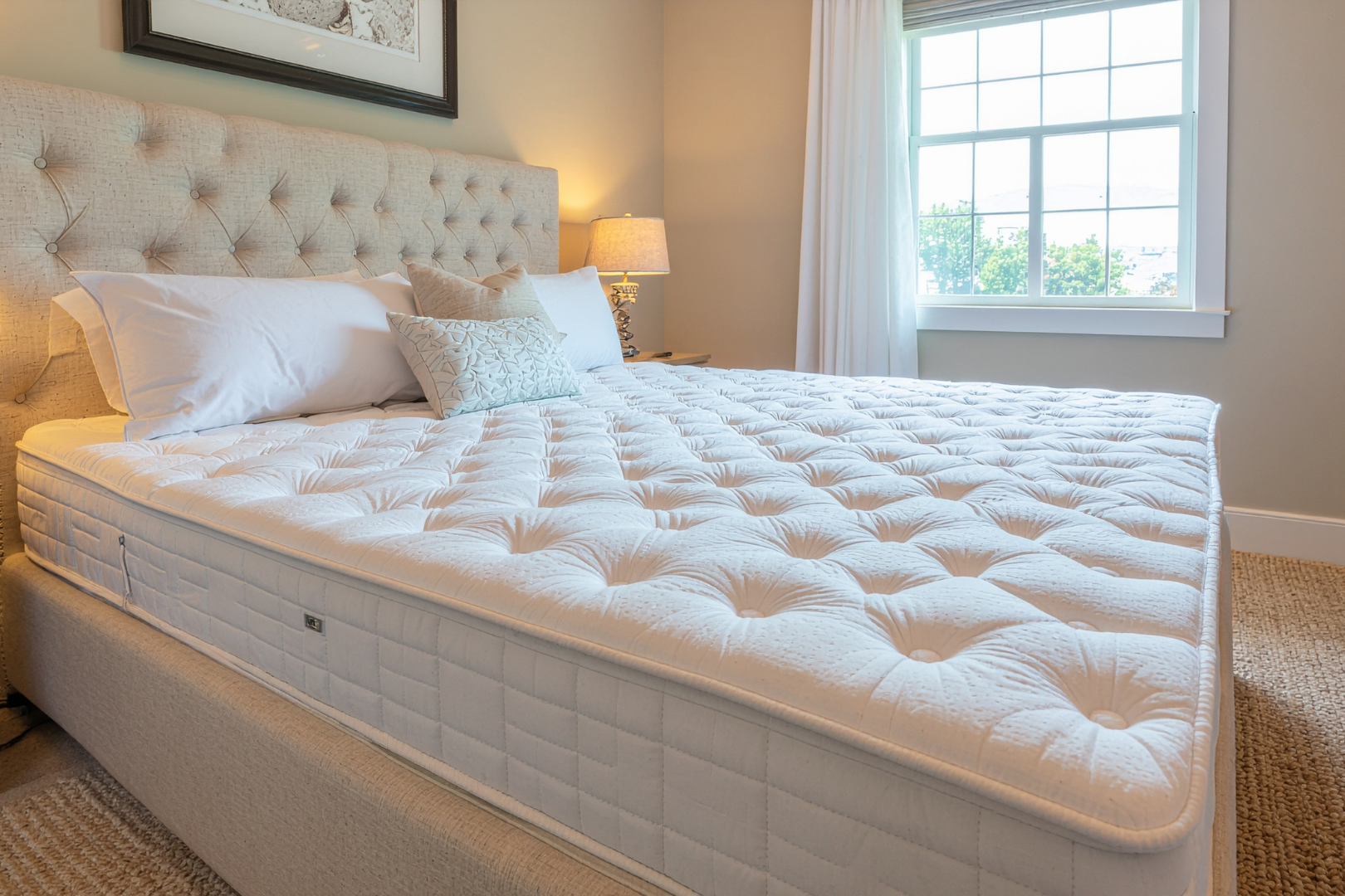 Bright bedroom with a tufted bed, white bedding, and a window beside a bedside lamp.