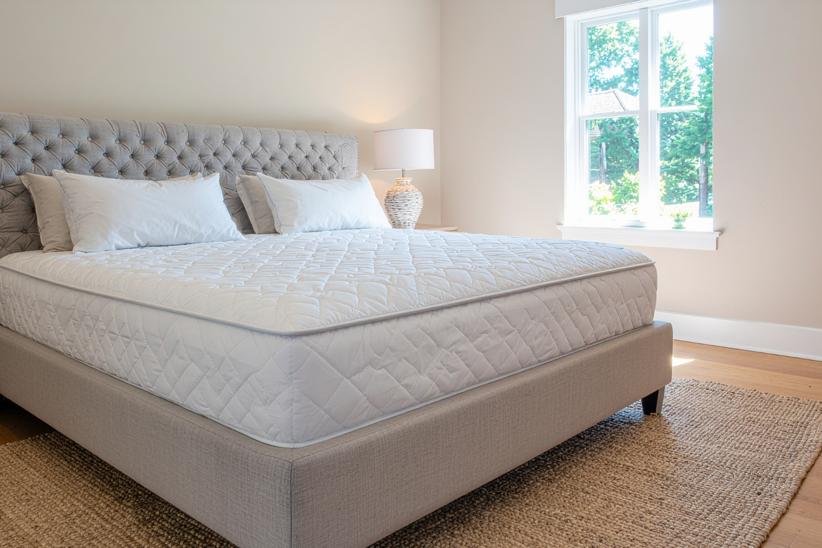 Neatly made gray upholstered bed in a bright bedroom beside a window