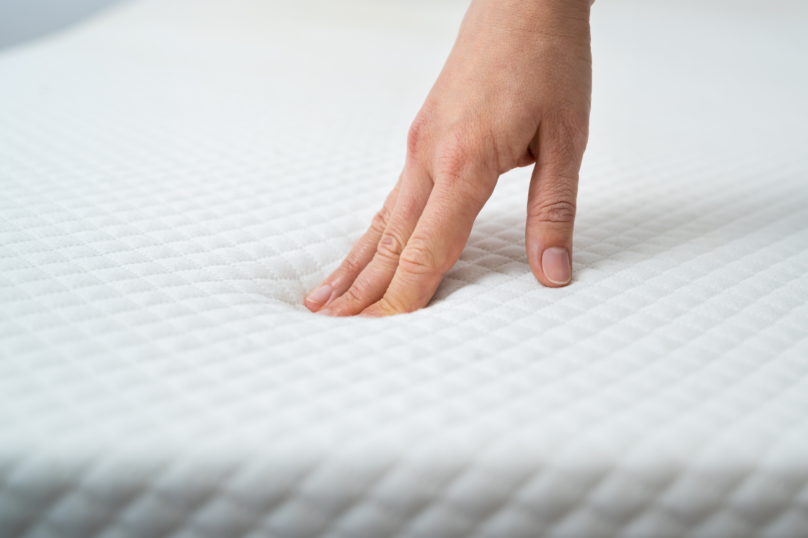 Hand pressing into a white memory foam mattress, showing softness and support