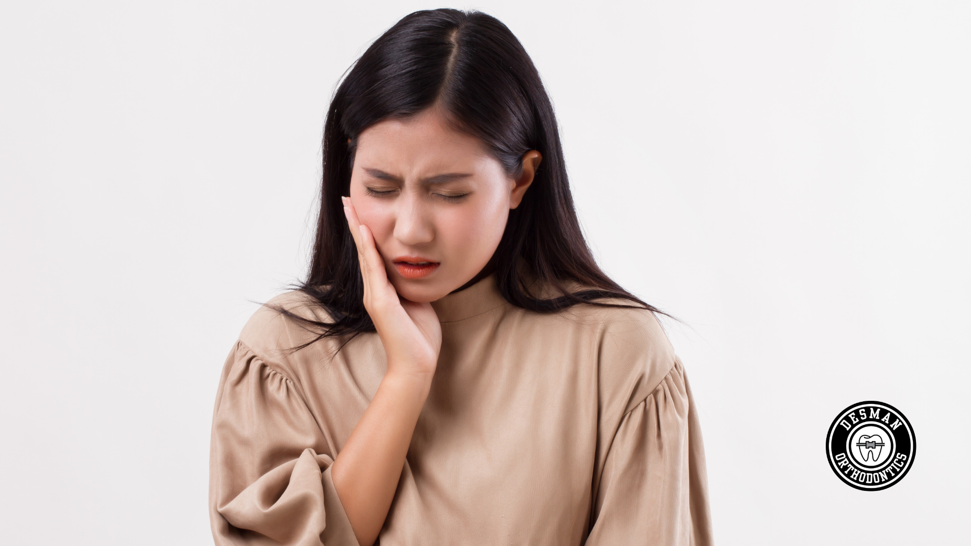 Woman holding her cheek with eyes closed, showing facial pain against a plain white background