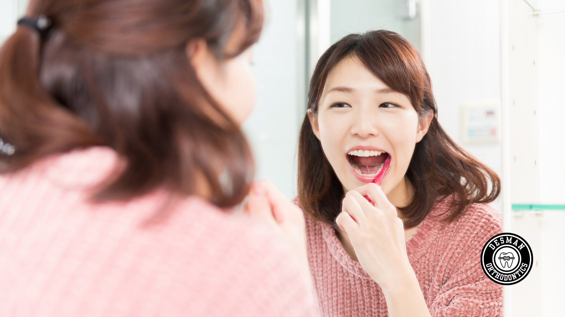 Woman applying lipstick while looking in a mirror in a bright room