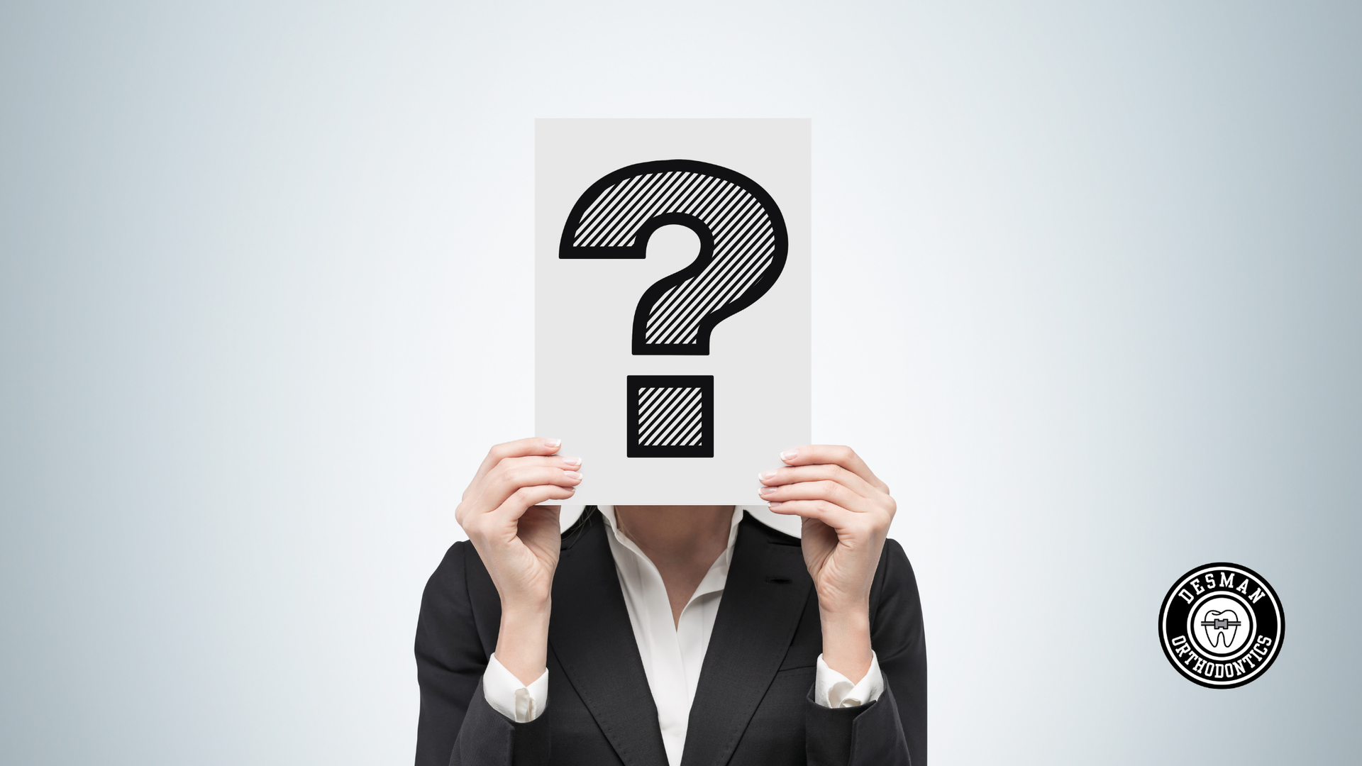 Person in a suit holds a sheet with a large question mark in front of their face