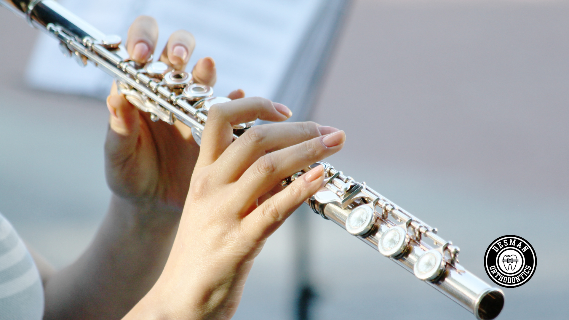 Hands playing a silver flute against a blurred light background