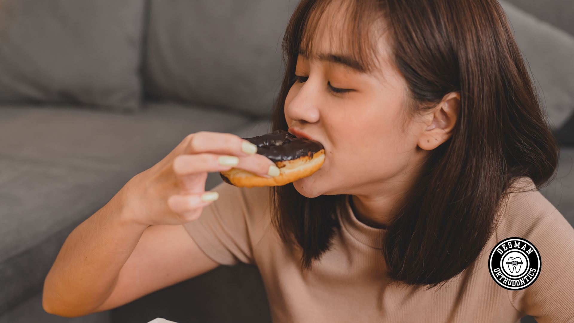 Woman taking a bite of a donut while seated on a gray couch