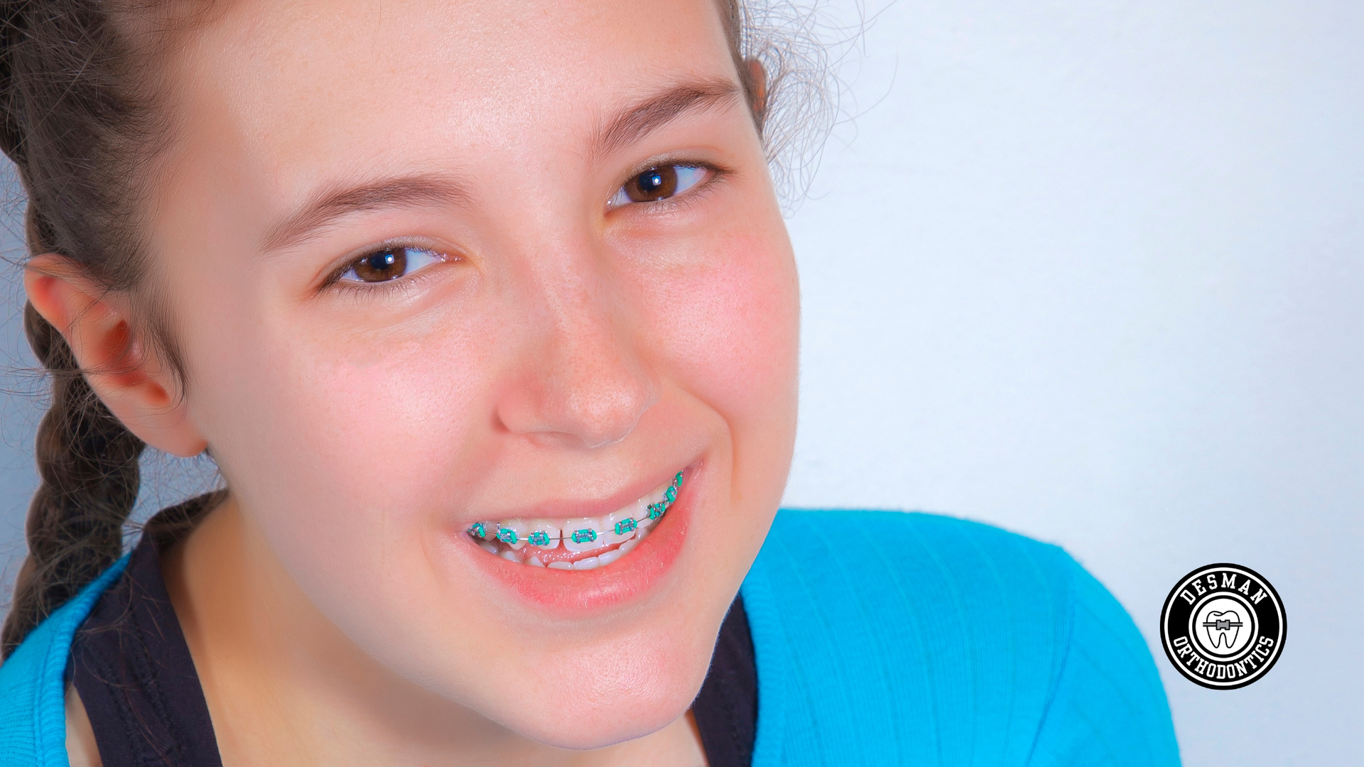 Smiling person with blue braces, wearing a blue shirt against a light background.