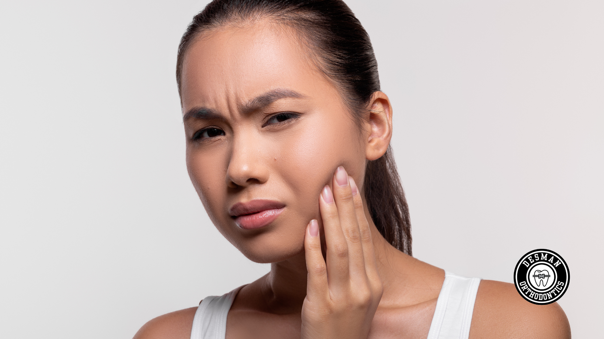 Woman touching her cheek with a pained expression, suggesting jaw or tooth pain.