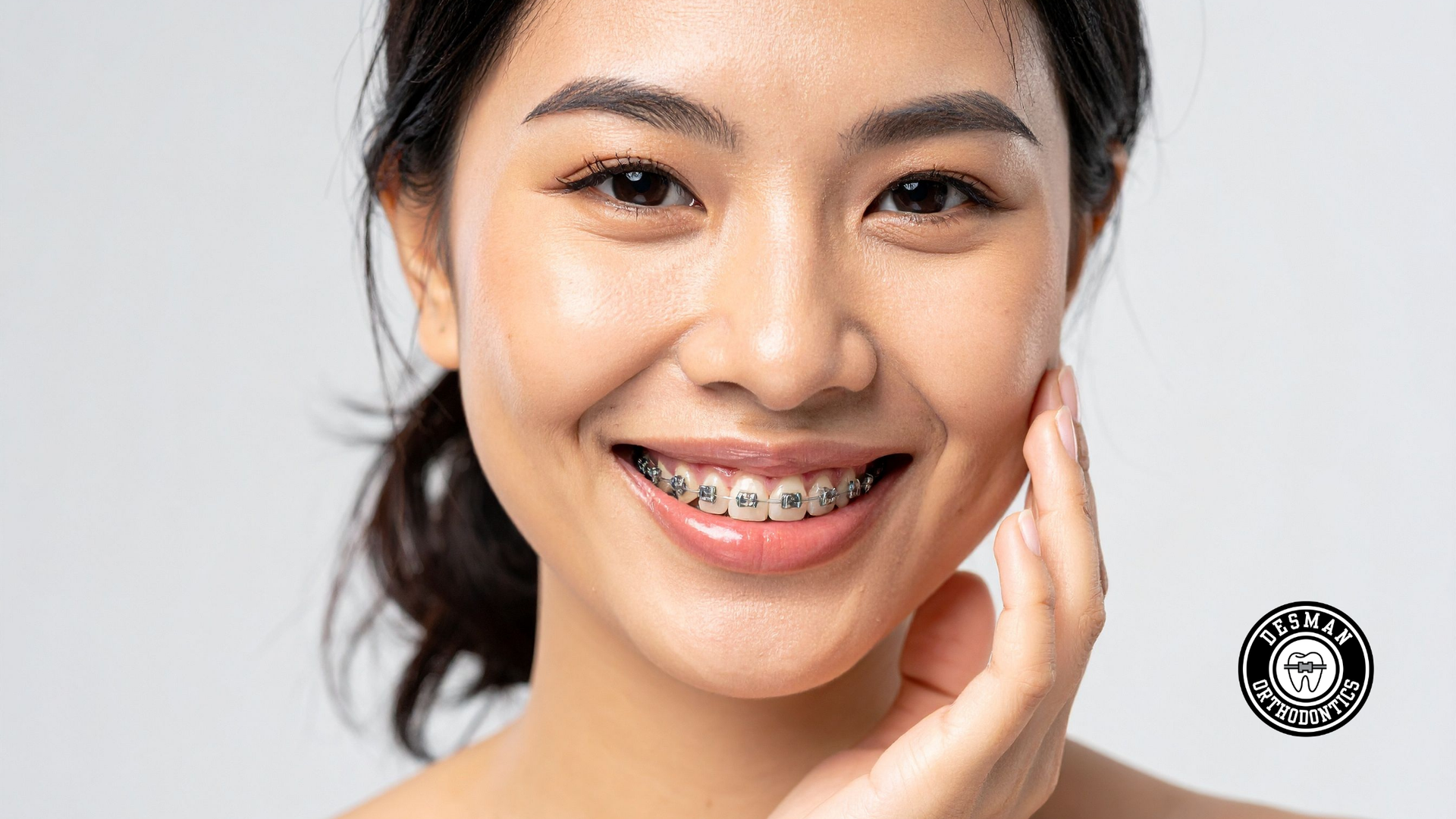 Smiling person with braces touching their cheek against a light background