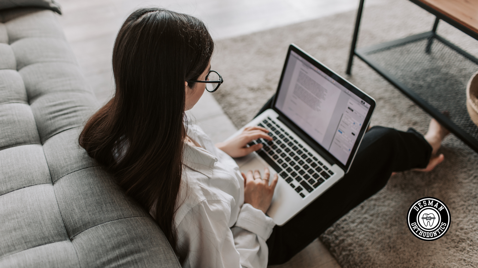 Person using a laptop on a gray couch in a bright living room
