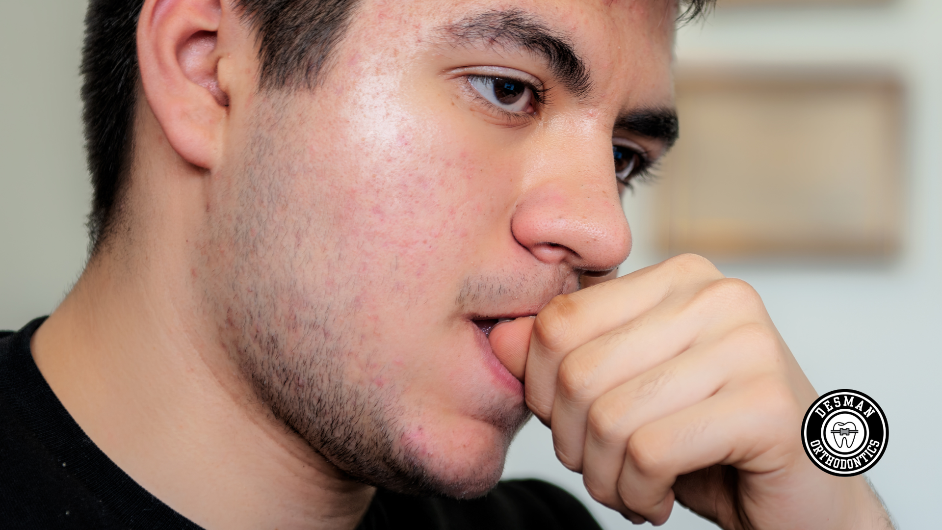 Close-up of a man resting his hand against his mouth, looking thoughtful indoors