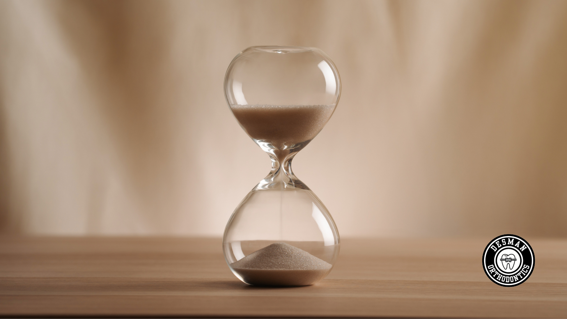 A glass hourglass on a wooden surface, with sand mostly collected in the bottom bulb.