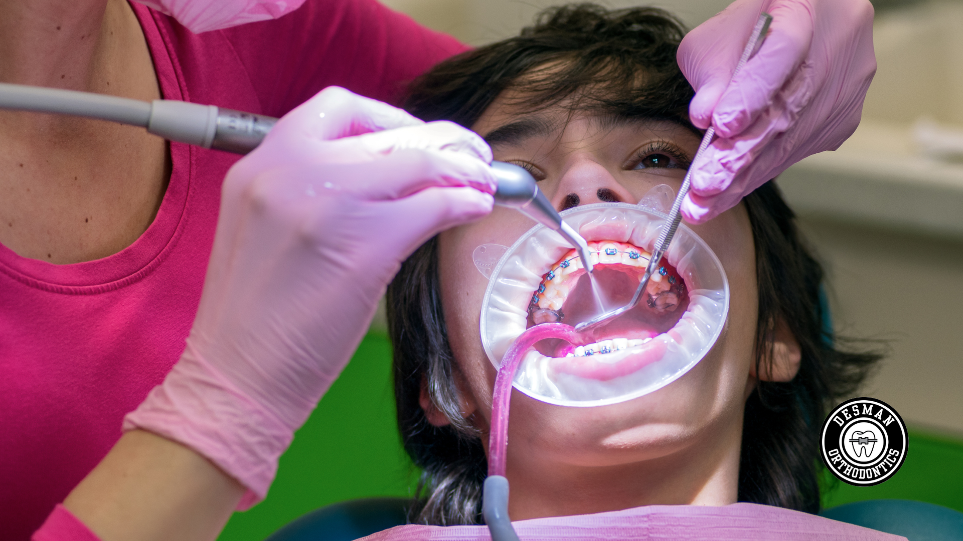 Dentist using tools on patient’s open mouth while wearing pink gloves and mask