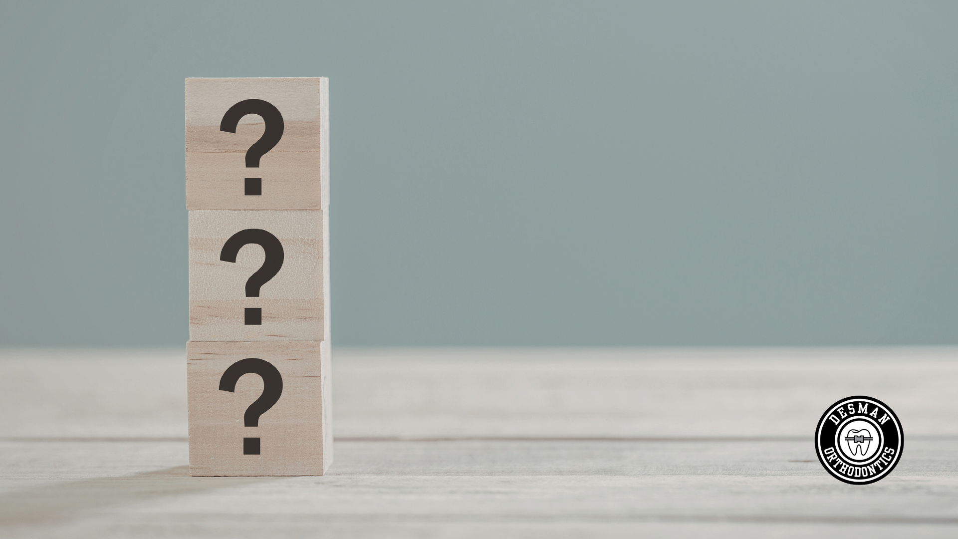 Wooden block with three question marks on a light tabletop against a pale blue background