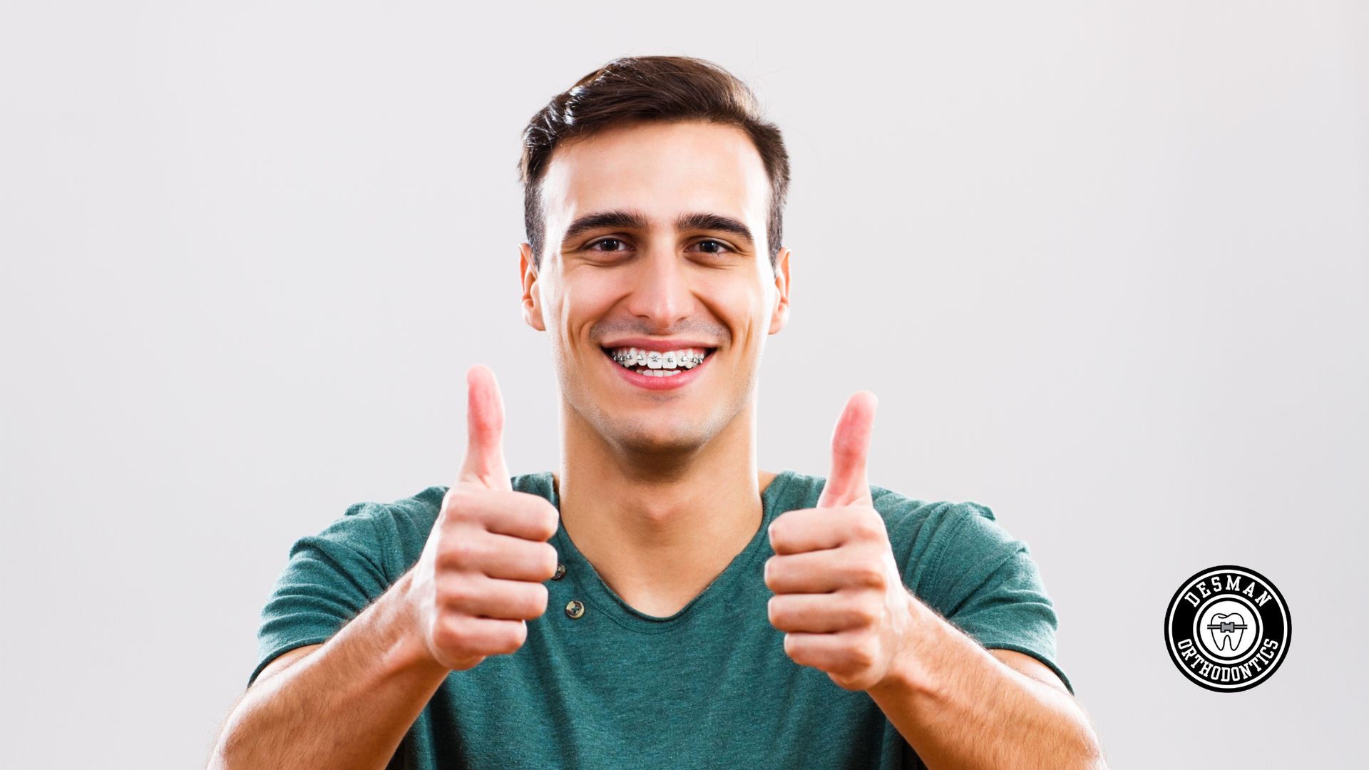 Smiling man in a green shirt giving two thumbs up against a light background
