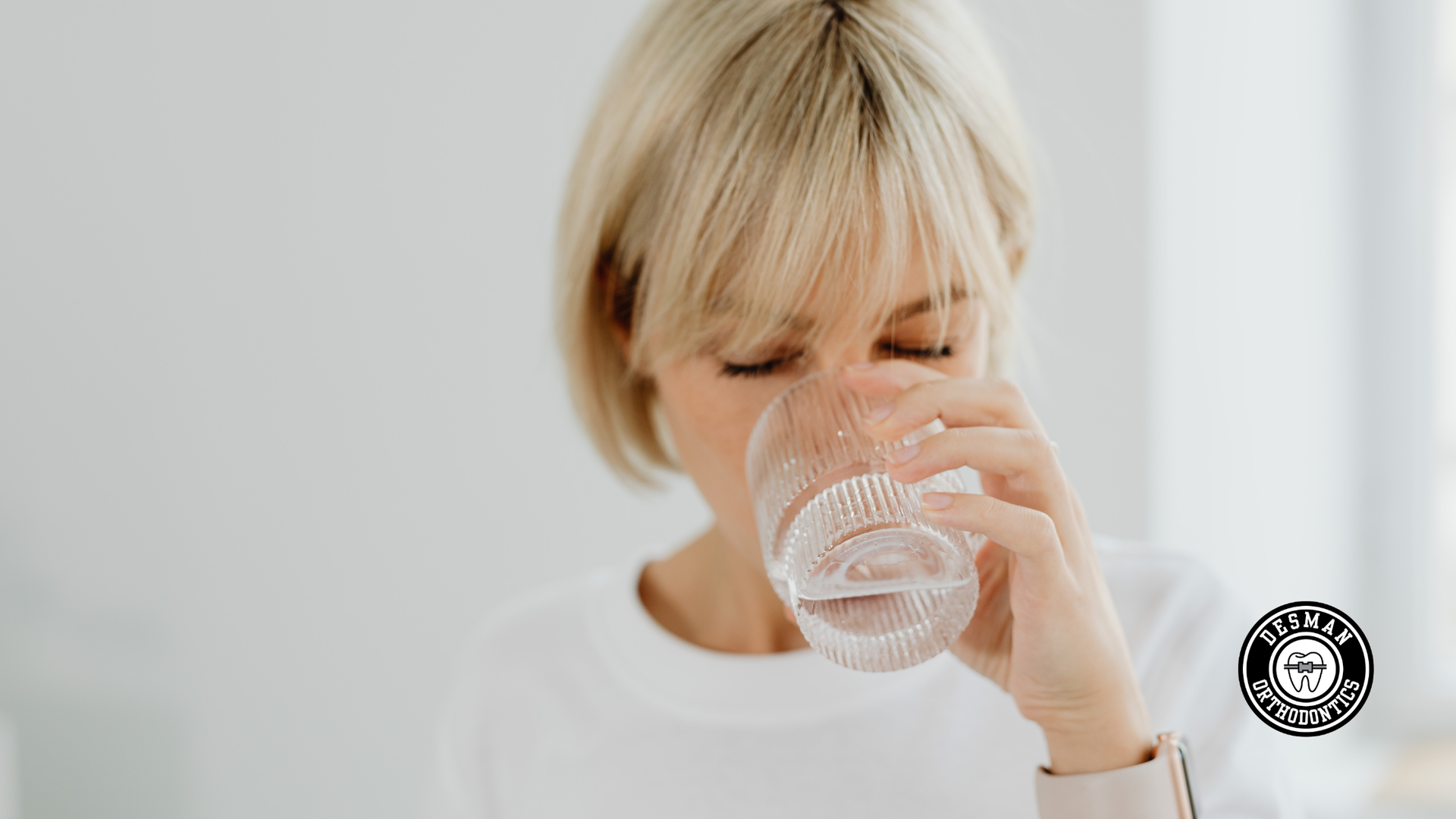 Person with blond hair drinking from a glass of water against a white background