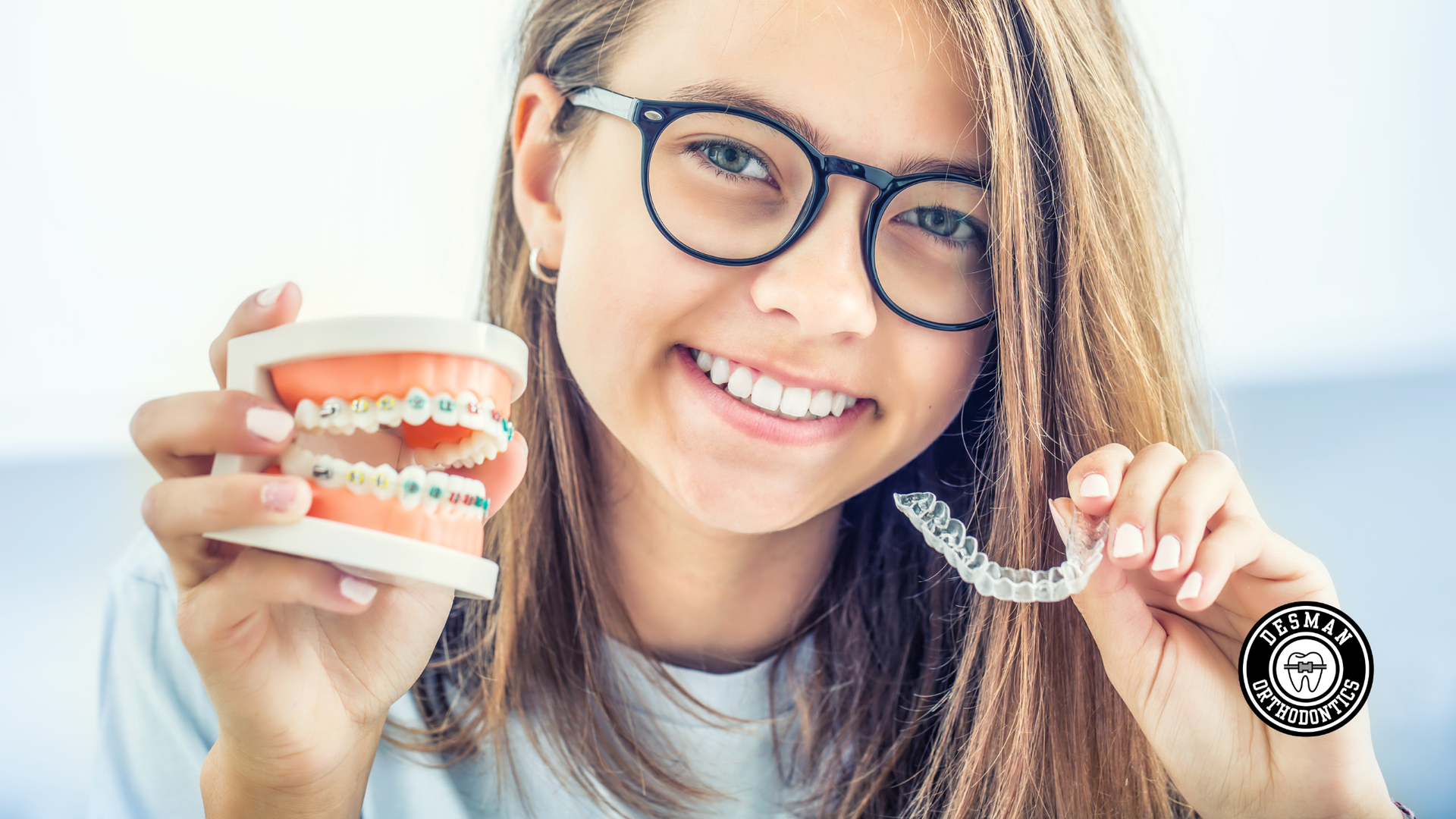 Smiling woman with glasses holding a dental model and clear aligner against a white background