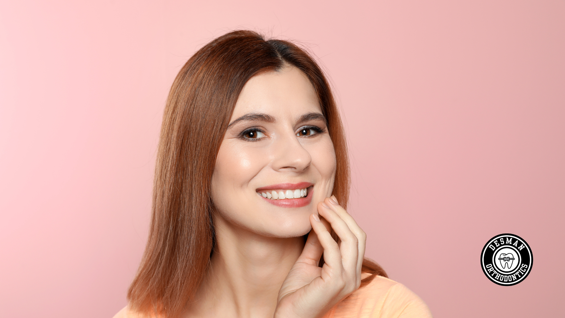 Smiling woman with red hair touching her chin against a pink background