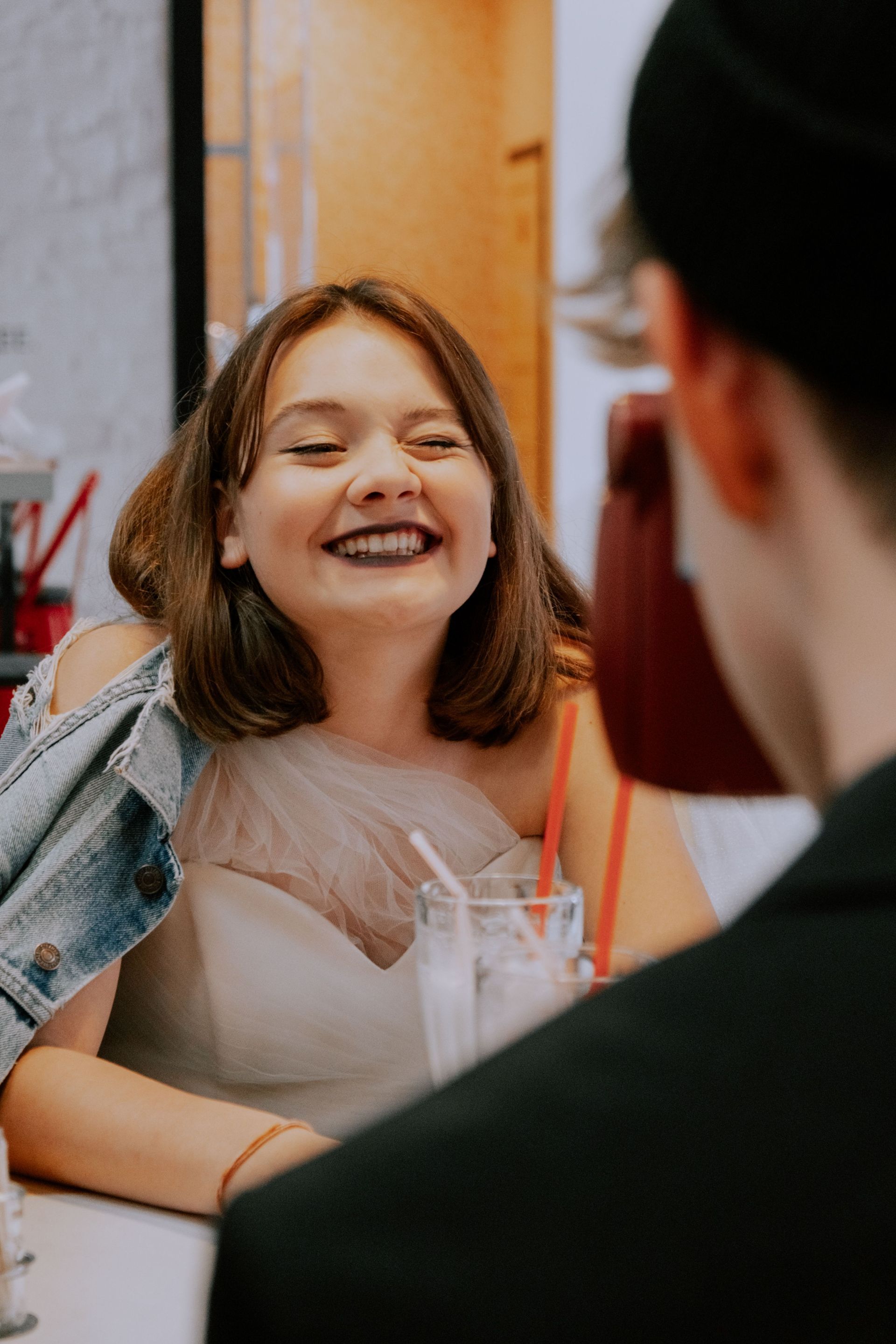 Smiling woman in a denim jacket chatting at a table with a drink in a café