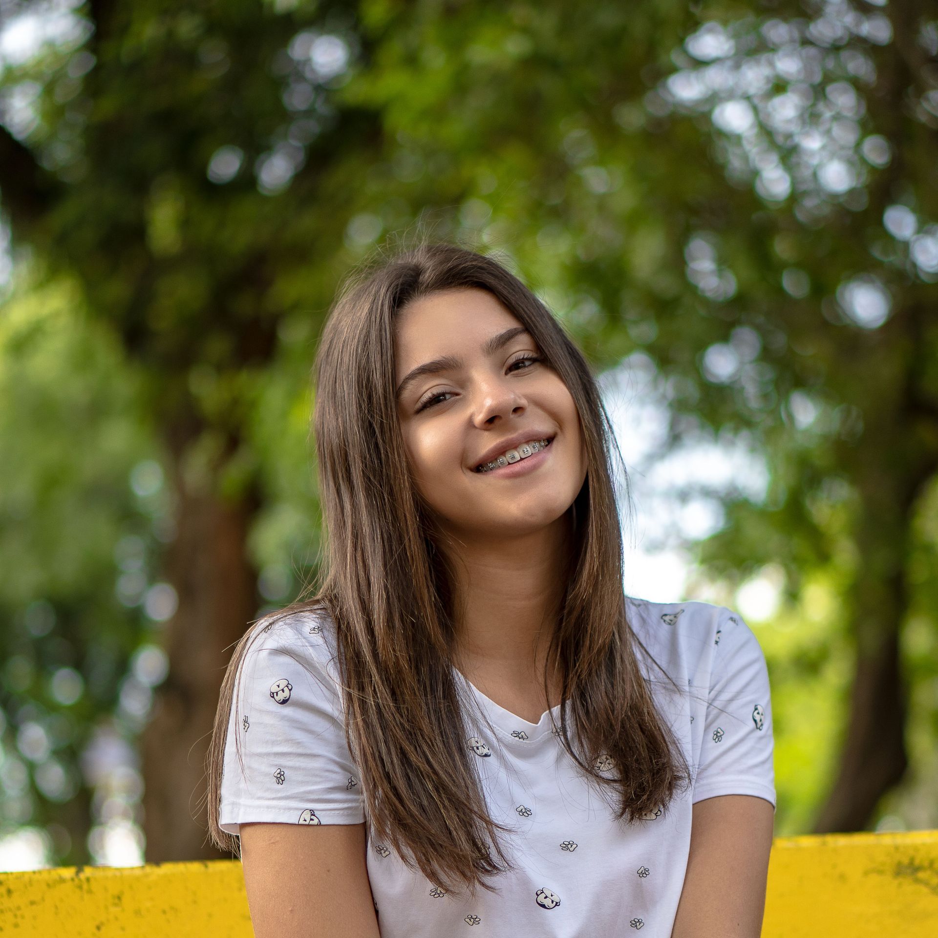 Smiling person in a white shirt sitting outdoors with trees in the background