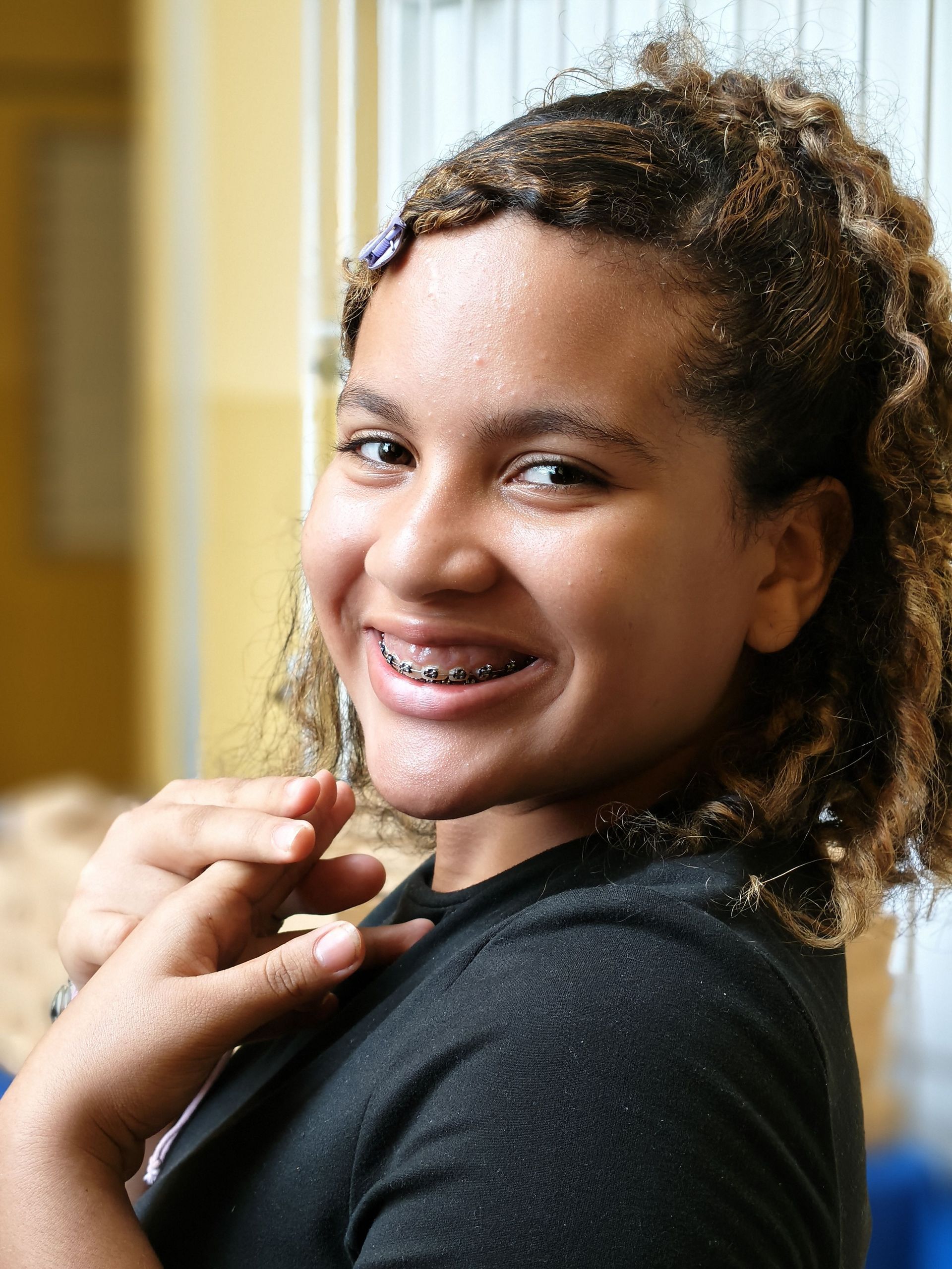 Smiling person with curly hair holding a necklace in a warm indoor setting