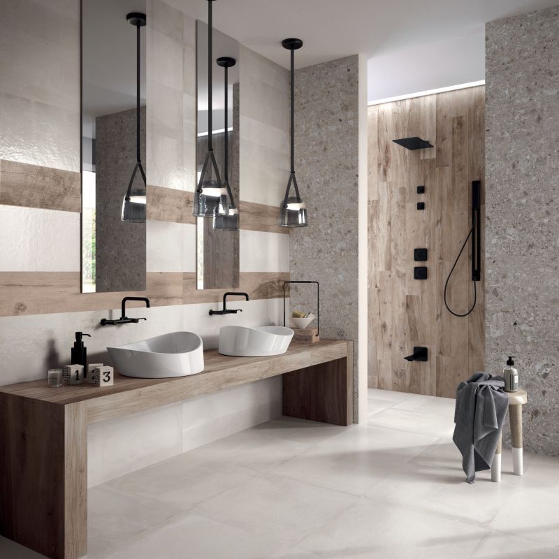 Bagno moderno color beige con doppio lavabo, specchi rotondi, lampade a sospensione e zona doccia in legno.