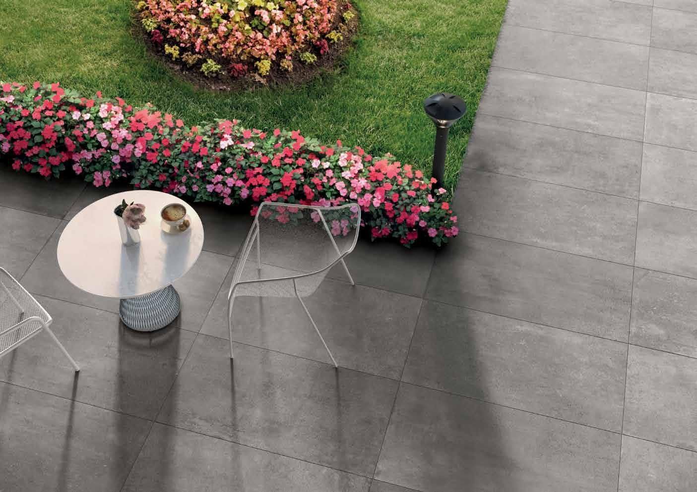 Patio con sedie trasparenti, tavolino rotondo, fiori rosa e pavimentazione in pietra grigia рядом
