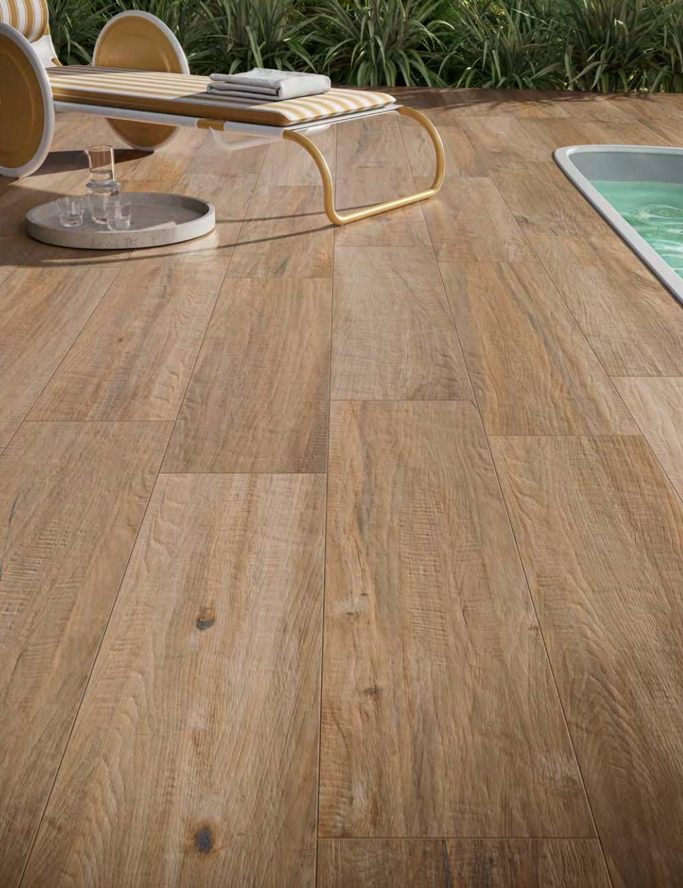 Terrazza in legno a bordo piscina con lettini prendisole.