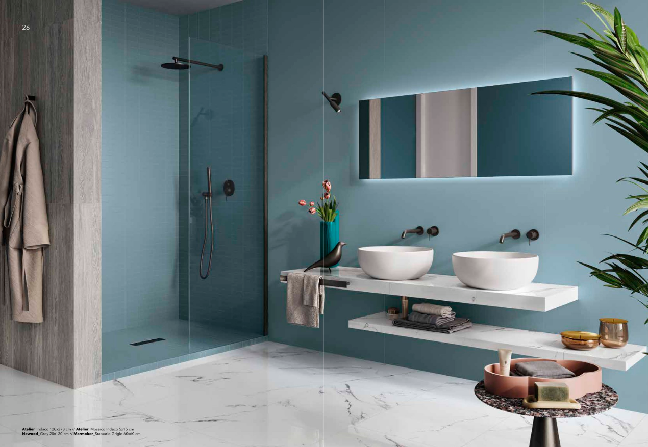 Bagno moderno con doccia in vetro blu, lavandini bianchi, mobiletto sospeso e grande specchio.