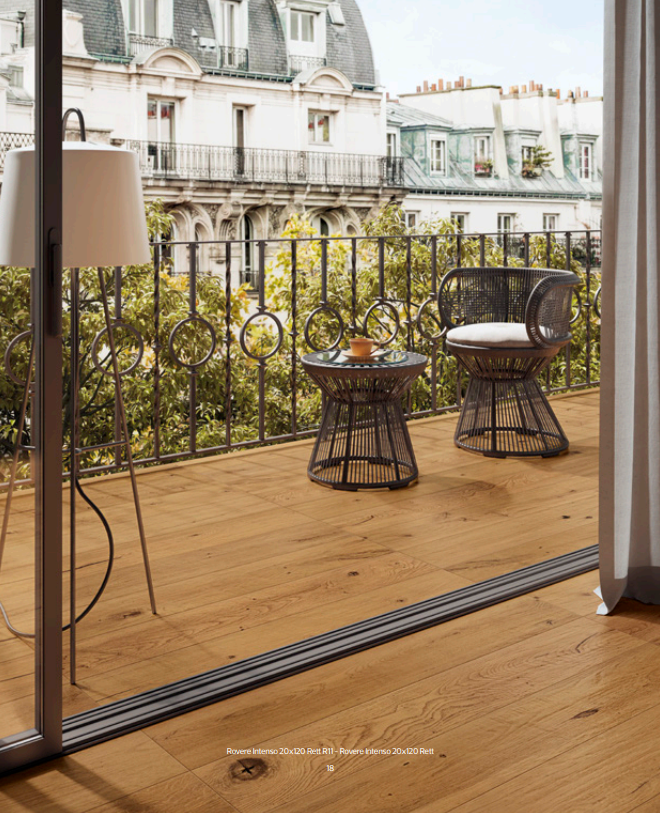 Balcone con pavimento in legno, due sedie e un tavolino con vista sugli eleganti tetti parigini.