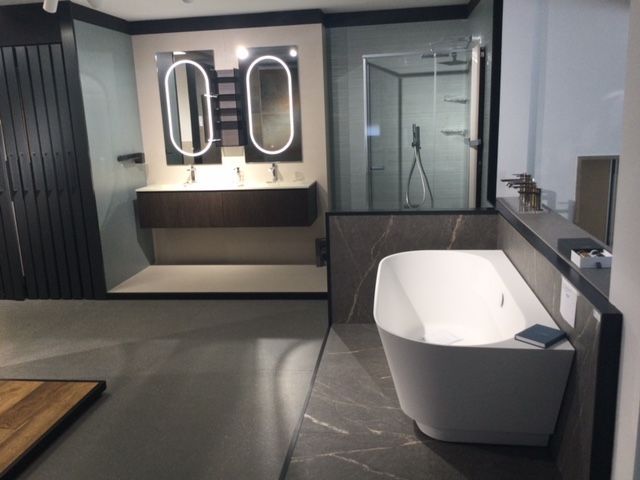 Bagno moderno con vasca freestanding, doppi specchi ovali e box doccia in vetro in un elegante interno grigio.